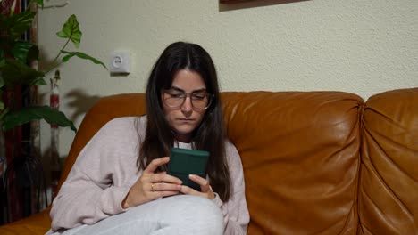 Mujer-Leyendo-Noticias-En-El-Teléfono-Móvil-Mientras-Está-Sentada-En-Un-Sofá-Marrón