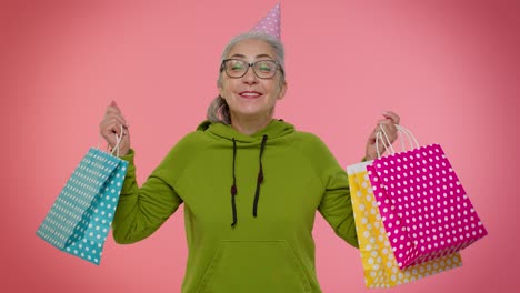 elderly granny woman showing shopping bags, advertising discounts, looking amazed with low prices