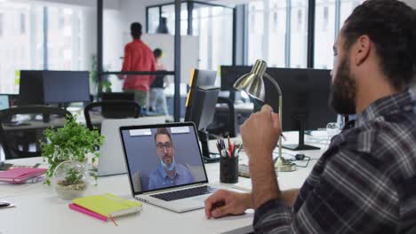 Middle-eastern-man-talking-on-video-call-with-male-office-colleague-on-laptop-at-office