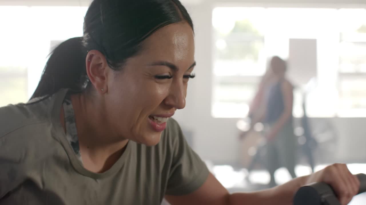 체육관에서 슬로우 모션으로 타원형 자전거를 타고 훈련하는 행복하고 확고한 백인 여성