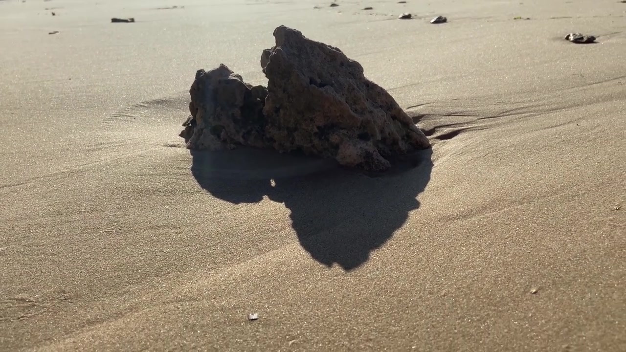 Sollys på en sten på en sandstrand med en person, der går