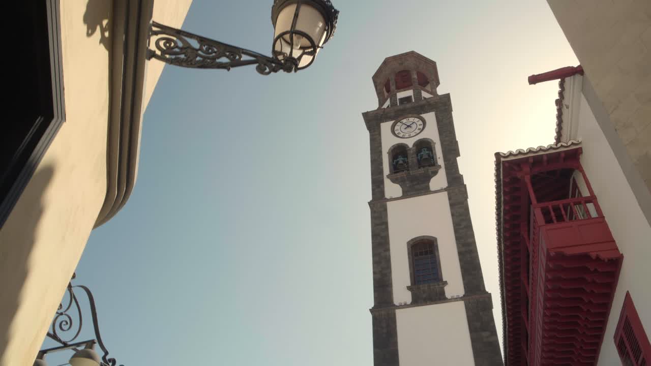 Architettura tradizionale in pietra di un campanile di chiesa con un orologio accanto a un lampione stradale ornato a Santa Cruz de Tenerife. Inquadratura statica dal basso