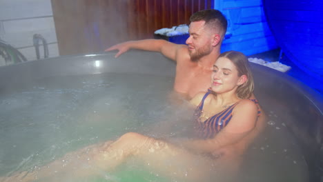 bearded man and blonde woman in stripy swimsuit sit in the hot tub. couple in love having spa time together. top view.