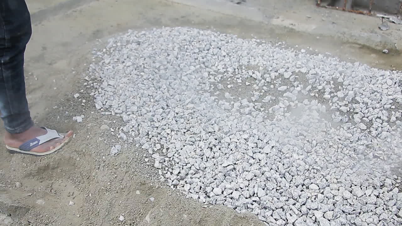 Indian mason worker pouring granite stones onto a mixed landfill site to level or enhance the surface
