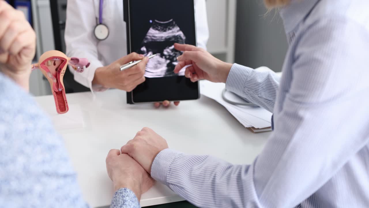 Gynecologist showing result of fetal ultrasound examination on digital tablet to married couple 4k