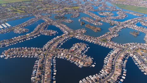 Man-made-dykes-create-waterfront-properties-at-the-Town-of-Discovery-Bay,-California---aerial-pull-back-tilt-down-reveal