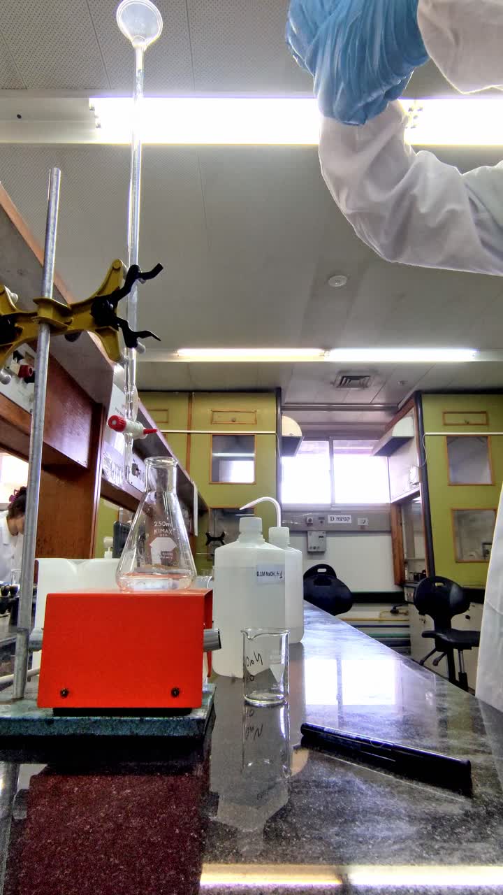 A man in a lab coat is wearing gloves and working with a beaker