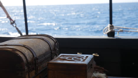 Antique-pirate-chest-and-carved-Celtic-viking-box-on-a-boat,-sea-glittering-in-the-background