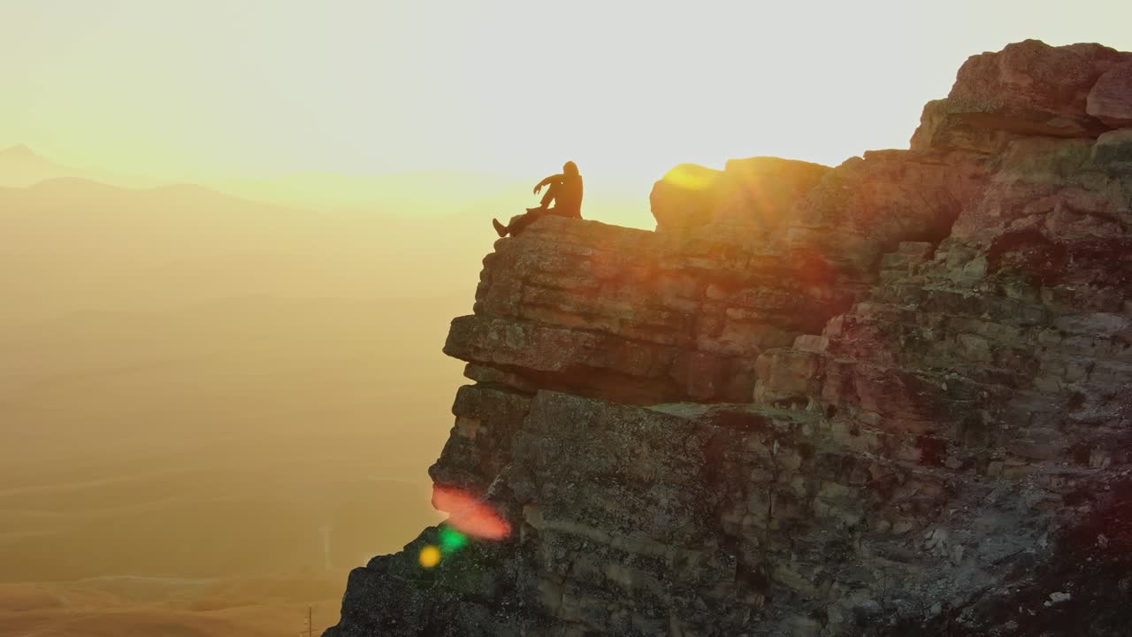 vista aérea. un hombre se sienta en una roca en el fondo del valle lleno de puesta de sol y las siluetas de las montañas. el avión no tripulado vuela en círculo y los rayos de la puesta de sol dan luces brillantes. crimea.