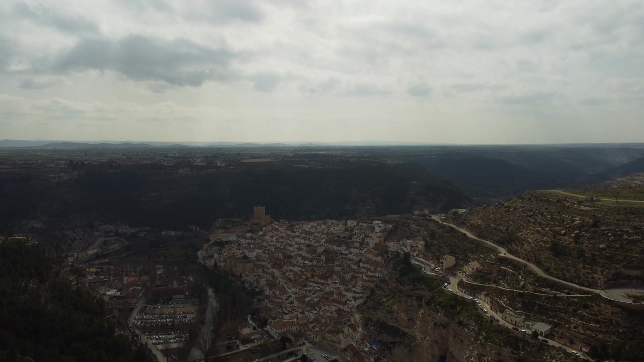 Discesa aerea con drone 4K, che rivela il drammatico villaggio di Alcalá del Júcar costruito nella parete di una scogliera all'interno di un canyon, con il vasto altopiano della Castiglia-La Mancia sullo sfondo