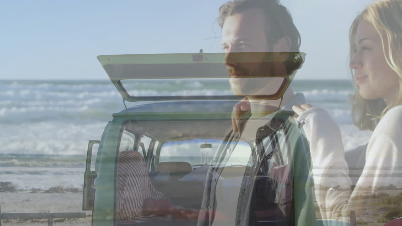 Viewing beach from open car trunk, couple watching animation on laptop