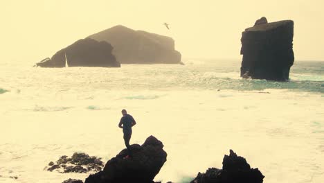 silueta de un hombre de pie en una roca con los brazos abiertos contra la playa de monsteiros en sao miguel, isla de las azores