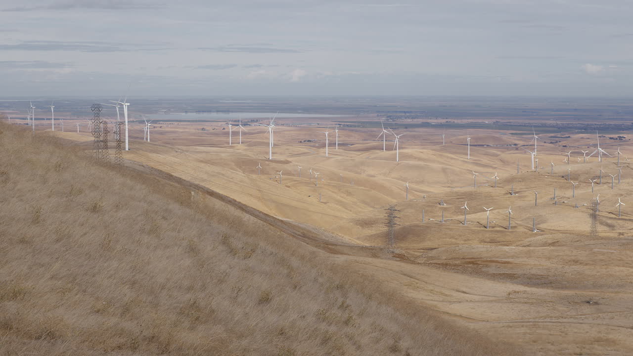 amplia toma de colinas secas con molinos de viento girando en el fondo en un día nublado