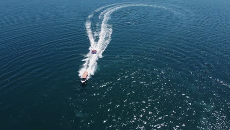 Aerial:-Tourists-enjoying-a-bumpy,-fun-ride-towed-by-motorboat-in-sea