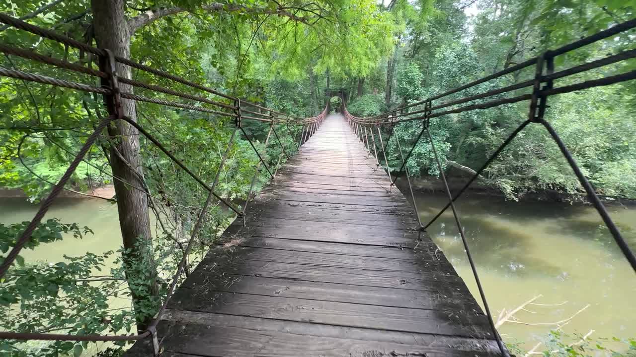 공원의 개울 위에 있는 흔들 다리를 건너는 모습