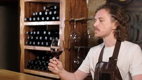 authentic shot of successful male sommelier is tasting a flavor and checking white wine quality poured in transparent glass in a wine cellar.