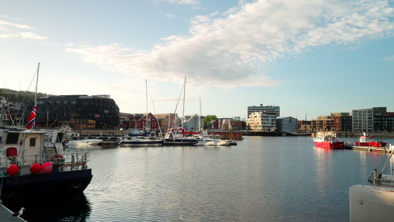 Fishing boats and sailboats docked at Tromsø harbor with waterfront buildings illuminated by the Arctic midnight sun during summer in northern Norway