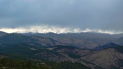 Gewitterwolken-Verdecken-Schneebedeckte-Felsige-Berggipfel,-Die-über-Immergrünen-Bäumen-In-Colorado-Aufragen