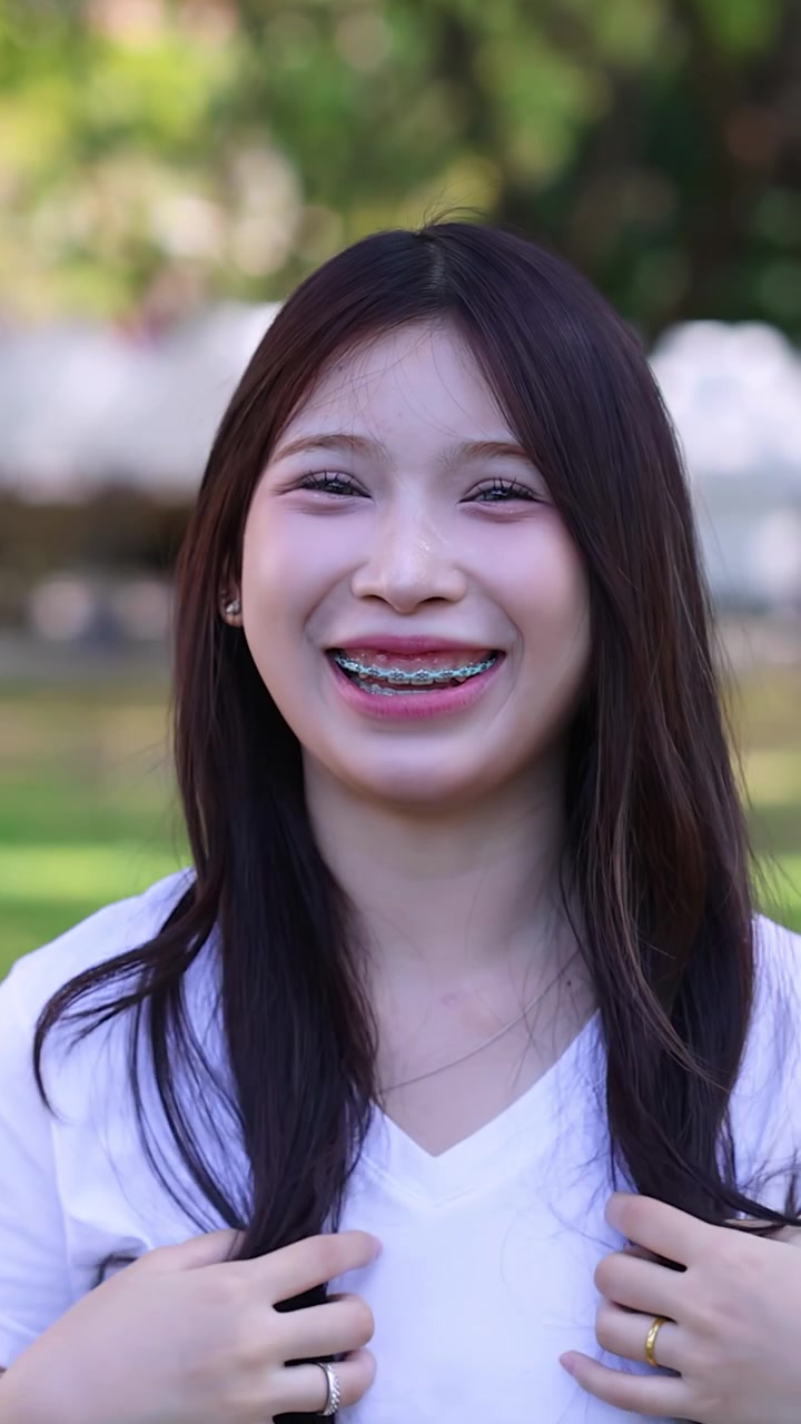 ผู้หญิงเอเชียร่าเริงที่จัดฟันกำลังหัวเราะและยิ้มระหว่างการถ่ายภาพบุคคลกลางแจ้งที่สดใส