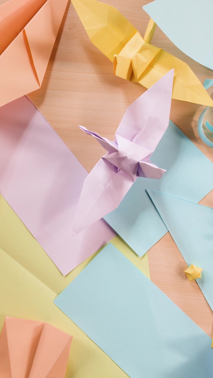Top-down view of hands organizing various pastel origami figures and paper scraps on wood