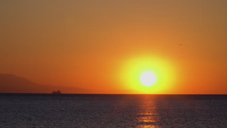 Beautiful-static-shot-of-a-sunrise-with-boat-and-mountains-on-horizon