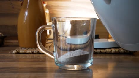 Taking-electric-kettle-and-pouring-hot-boiled-water-on-instant-coffee-powder-in-transparent-cup
