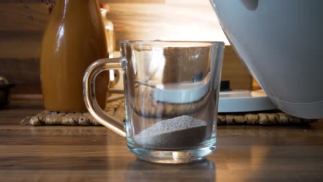 taking electric kettle and pouring hot boiled water on instant coffee powder in transparent cup