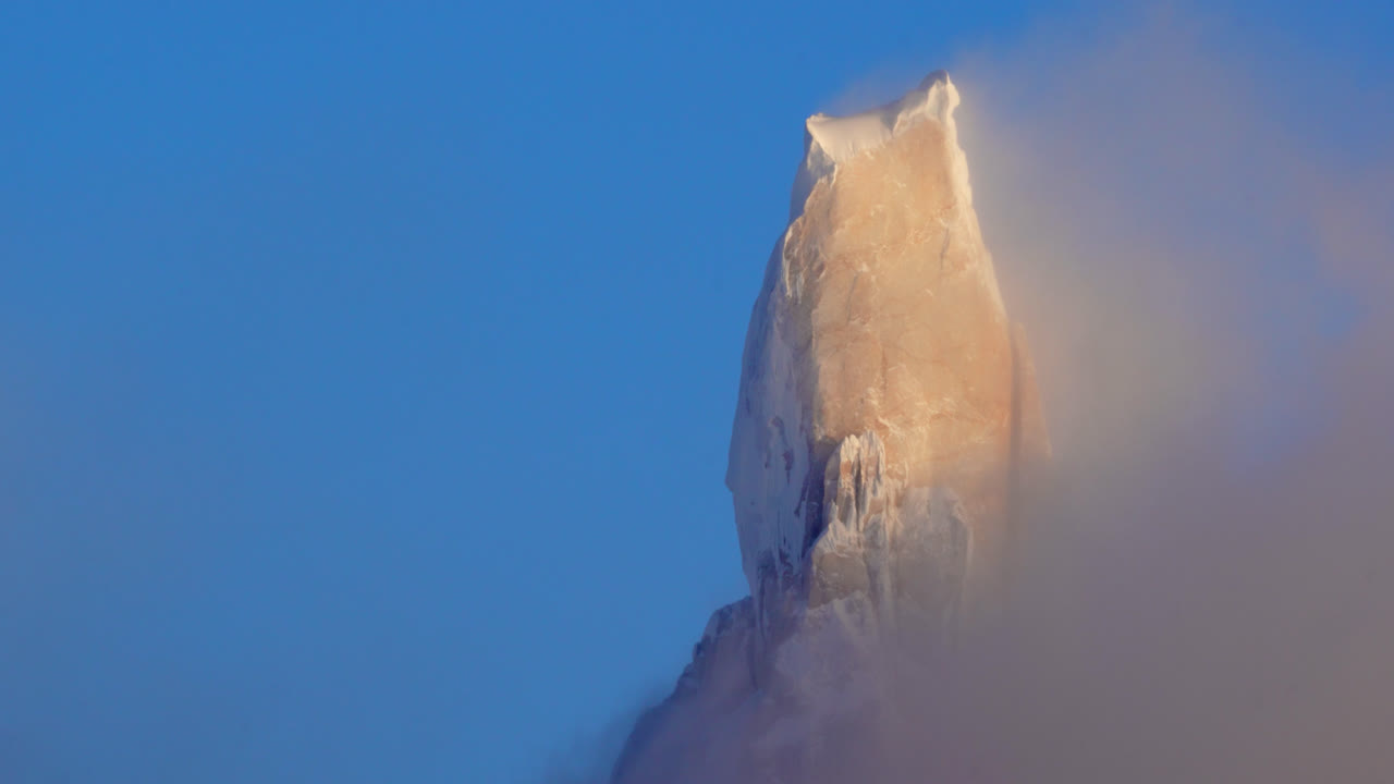 A majestic mountain peak emerges from clouds under a clear blue sky, creating a breathtaking view