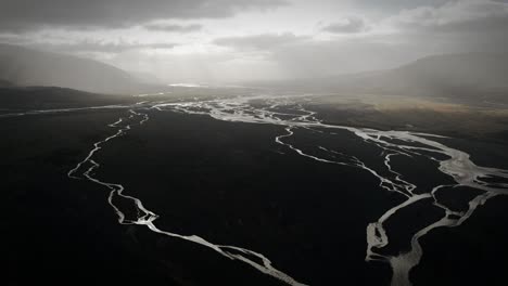 cinematic aerial thor valley, glacial river flowing through black volcanic floodplain, thorsmörk dramatic moody landscape iceland