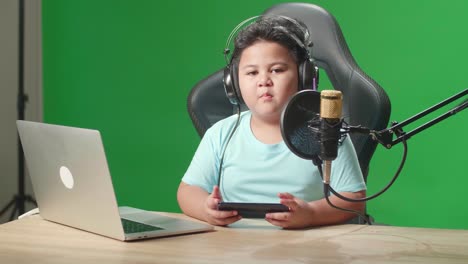asian little boy holding mobile phone and talking to camera while live stream on green screen
