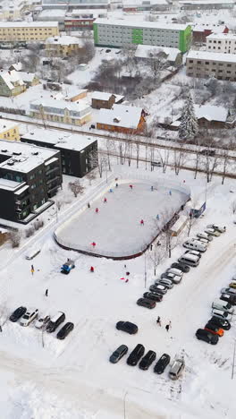 vertical drone shot circling a hockey game at a outdoor ice rink in a city