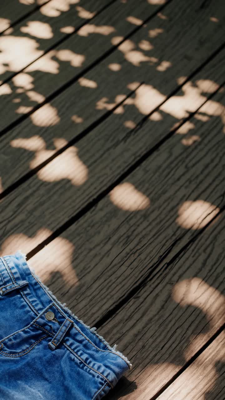 Top-down view of denim shorts on a wooden deck, with dappled sunlight creating playful shadows