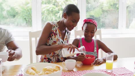 african american mother pouring milk in daughter's cereal bowl at home