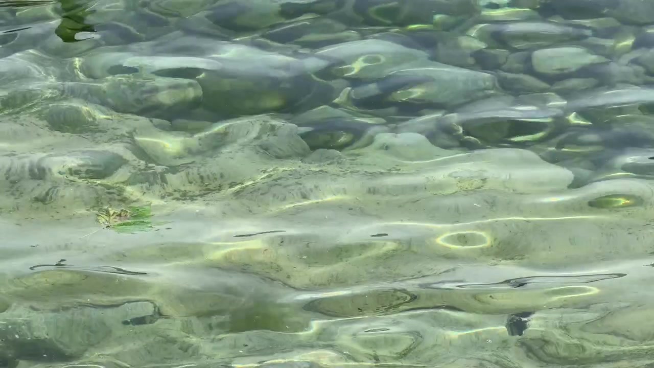 L'acqua trasparente del lago increspa un letto roccioso con la luce del sole che si riflette sulla superficie poco profonda.
