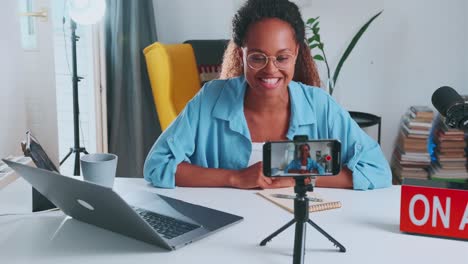 young african american woman blogger shoots video on phone sits in home office