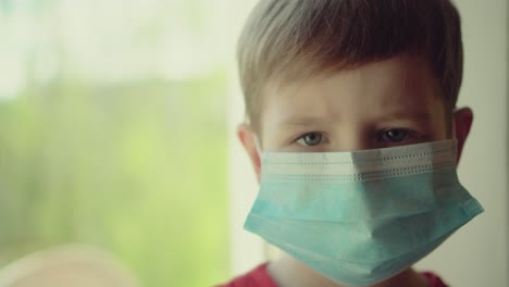 niño y su oso de peluche ambos en máscaras médicas de protección se sienta en el alféizar de la ventana y mira por la ventana 04