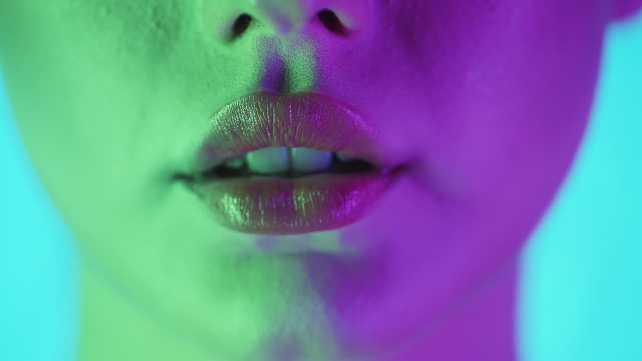 Extreme close up shot of a beautiful and attractive woman's lip as it slowly opens with lust and expectation with view of white teeth against turquoise background in slow motion