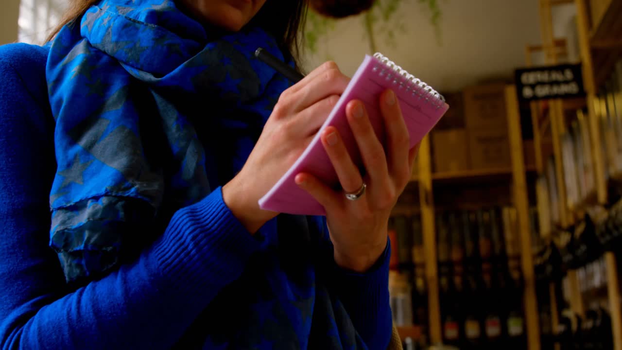 Giovane donna che scrive su un blocco note al supermercato 4k