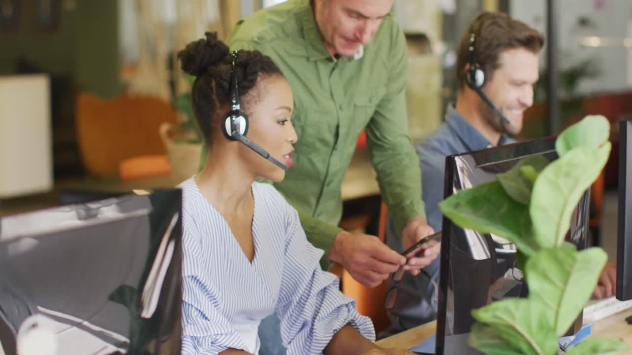 Happy diverse business people sitting at table and using phone headsets at office