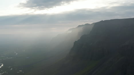 Aerial-panoramic-view-of-scenic-Icelandic-nature.-Flying-close-to-tall-mountains-with-sunrays-coming-trough-dark-clouds.