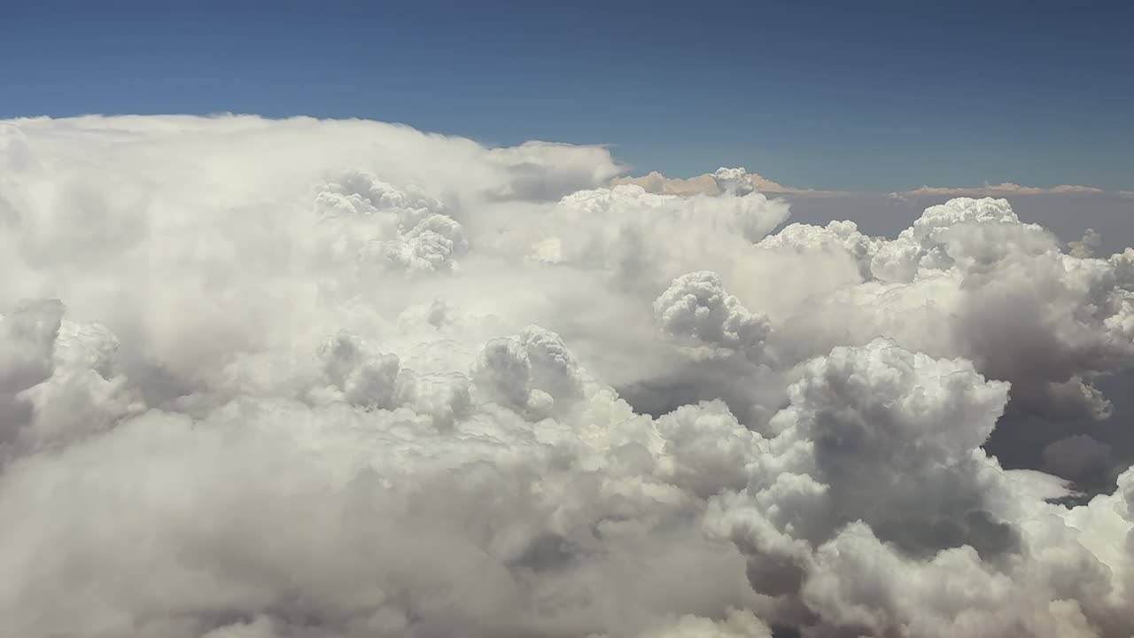 aerial view of a impressive front of cumulonimbus storm clouds as seen by the pilot of a jet flying at very high altitude at cruise, under a blue sky. High-contrast, hyper-realistic clouds.