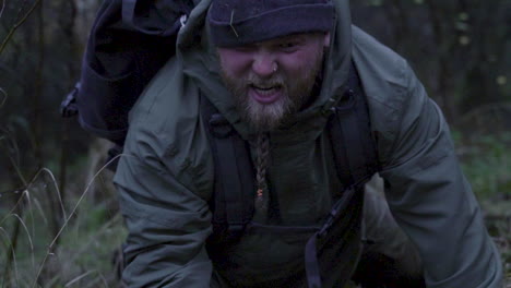 sad aggressive bearded man with dirty face standing up after falling down in forest