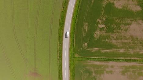 cenital drone shot following a camper van driving in middle of nordic farmlands