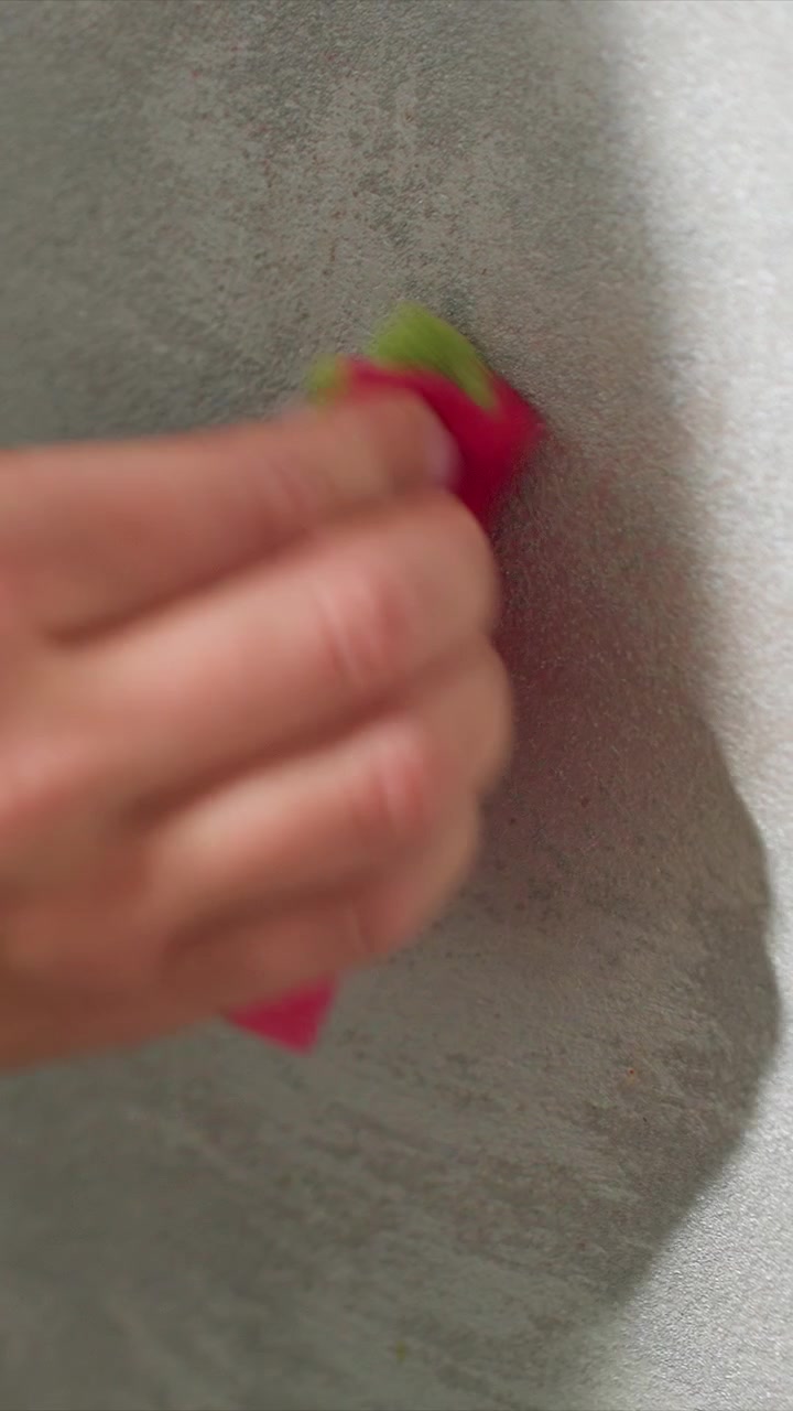 Close up of hand holding pink cloth wiping textured gray wall in consistent motion. Hand remains visible throughout cleaning surface with repetitive movement. Soft lighting highlights