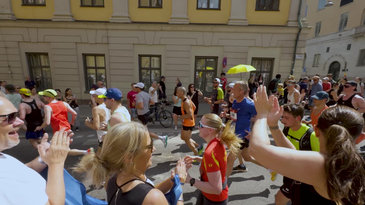 Runners pass cheering crowd at Stockholm Marathon on sunny day, slo-mo