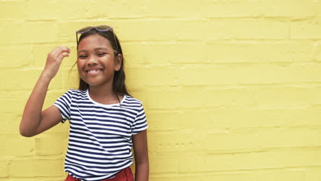 in school, a young biracial girl laughs against a yellow background with copy space