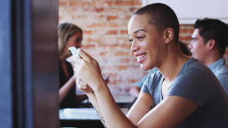 Mujer-Usando-Un-Teléfono-Móvil-Sentada-A-La-Mesa-En-Una-Cafetería