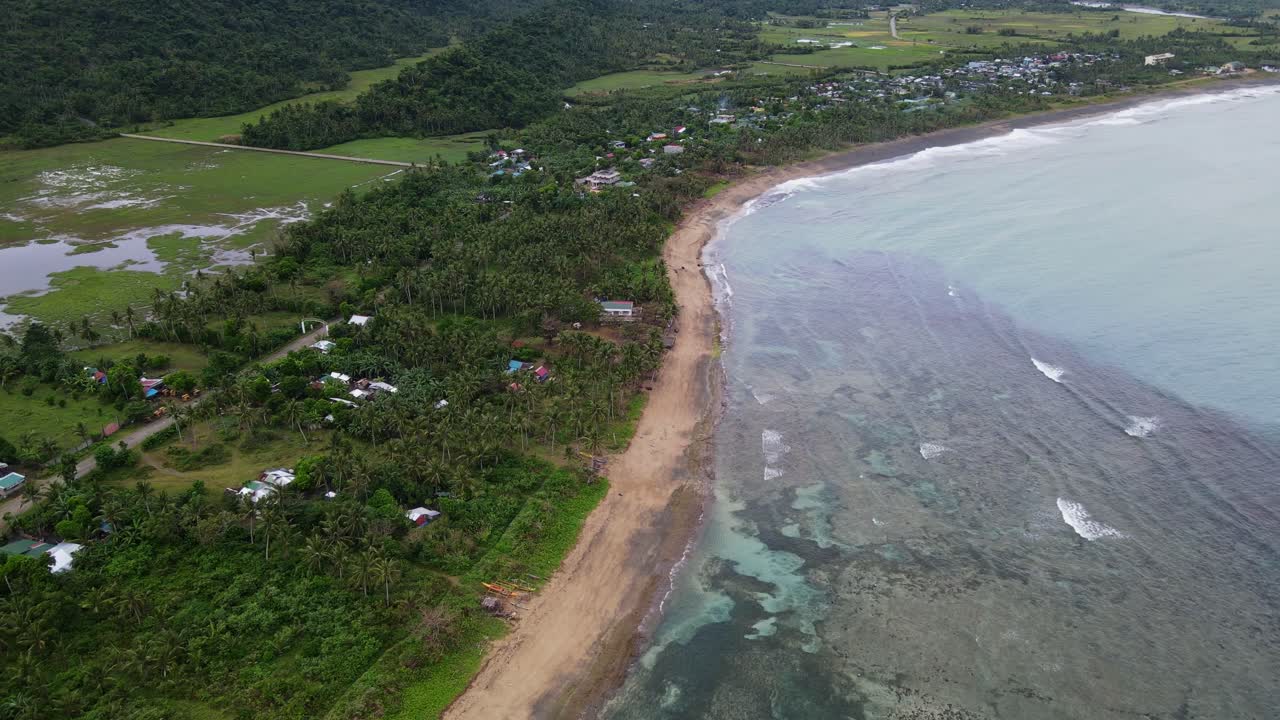 Aerial drone shot of peaceful tropical village coastline with lush greenery and idyllic crashing ocean waves at Virac, Catanduanes, Philippines