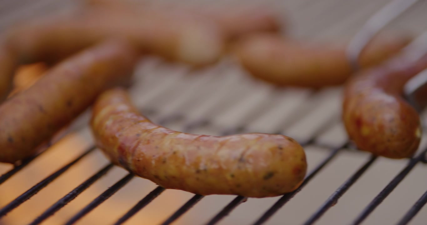 Salsicce che sfrigolano e si girano su una griglia calda per barbecue