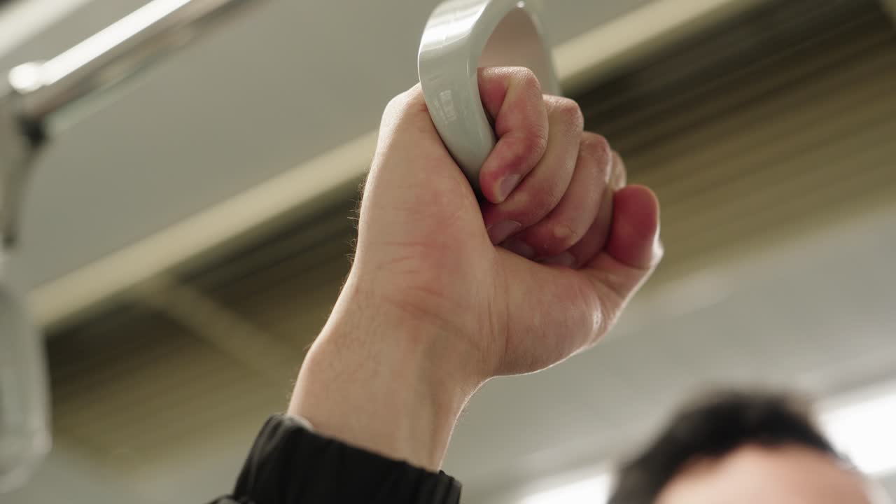 Close-up of a hand holding a subway strap inside a train during daily urban commute
